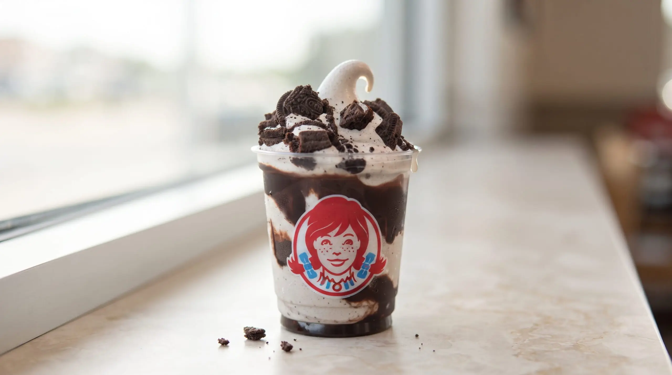 Close-up of Wendy's Oreo Brownie Frosty, Vanilla in a clear cup, topped with a swirl and Oreo pieces